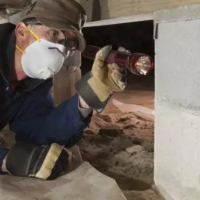 worker looking in crawlspace with flashlight